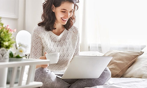 Frau mit Café und Laptop zu Hause auf dem Sofa